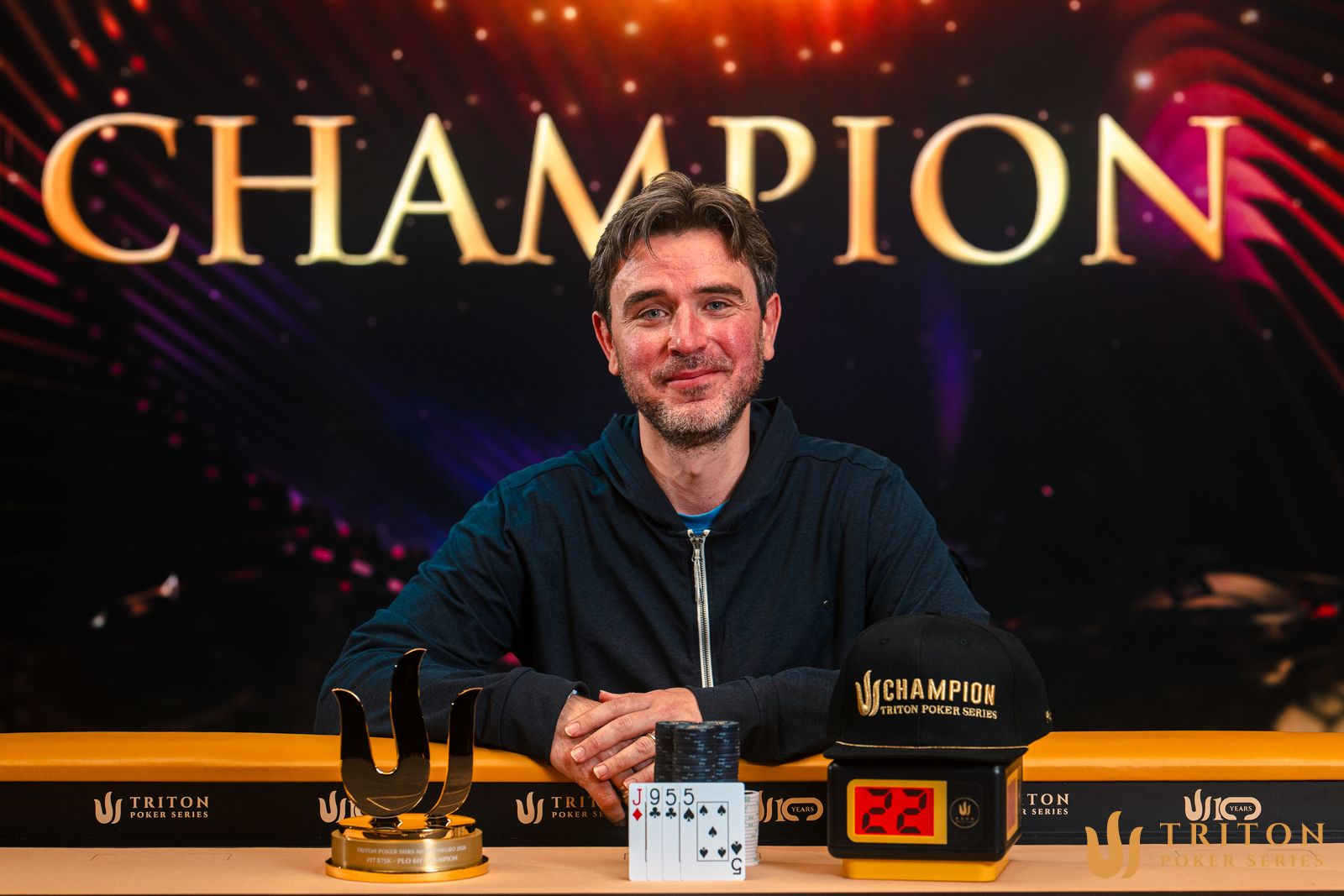 Zdjęcie przedstawiające graczy przy stole pokerowym podczas turnieju Triton Poker w Czarnogórze, z Richardem Gryko świętującym zwycięstwo.