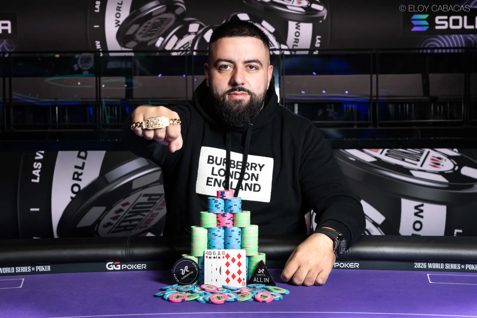 Daniel Aharoni pozuje z bransoletką WSOP i czekierm na tle stołu finałowego