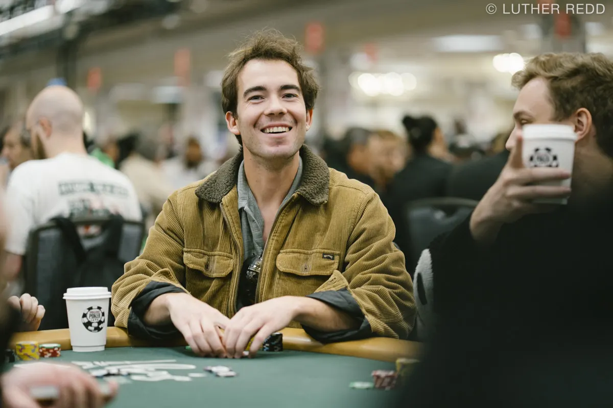 Gracze przy stole pokerowym podczas turnieju high roller, z widocznymi żetonami i kartami.