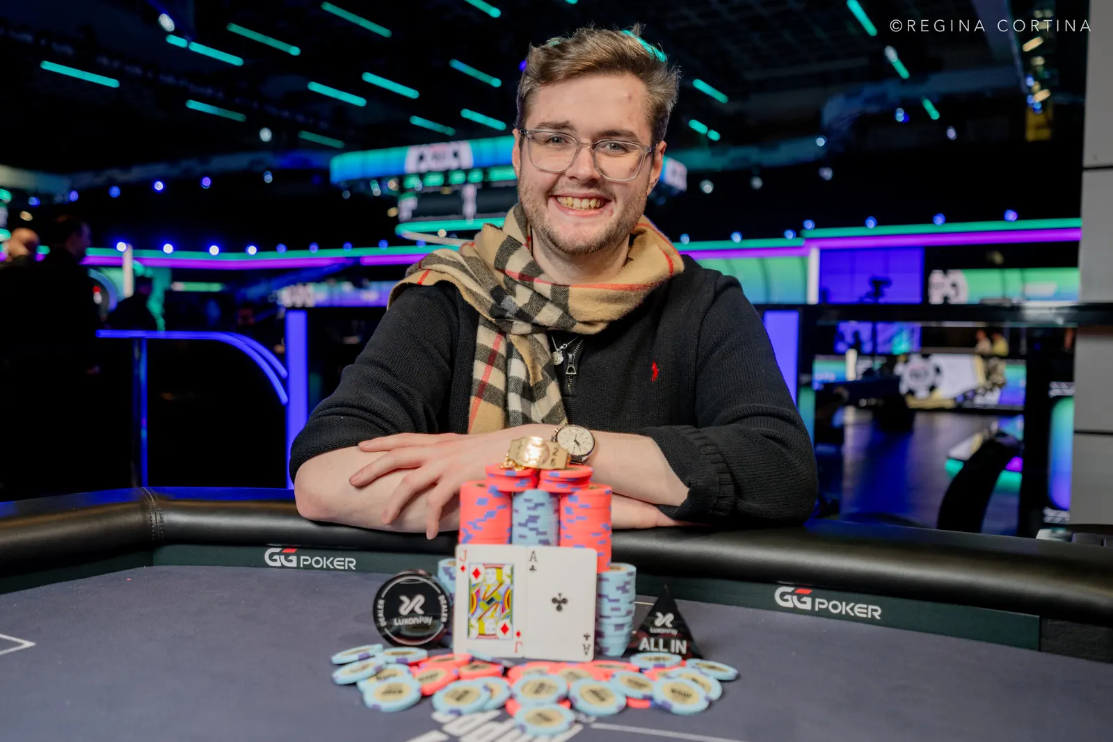 Uśmiechnięty Jamie Dwan trzymający złoty medal WSOP i czek o wartości ponad 2 milionów dolarów, siedząc przy stole pokerowym.